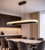 Modern oval LED pendant light with black frame and warm white illuminated diffuser suspended above a luxury dining table.