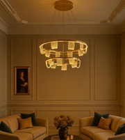 Ophelia Gold chandelier glowing warmly above beige sofas in a luxury sitting room.