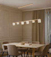 Straight bar acrylic chandelier with warm LED light above a wooden dining table