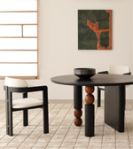 Modern round black dining table with sculptural legs, cream upholstered chairs, and minimalist decor.