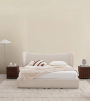 Modern beige upholstered bed with neutral bedding, wood nightstands, floor lamp, and plush rug
