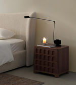 Modern bedroom with beige upholstered bed, wooden nightstand, black table lamp, and candle