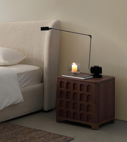 Modern bedroom with beige upholstered bed, wooden nightstand, black table lamp, and candle