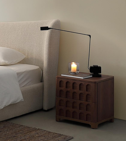 Modern bedroom with beige upholstered bed, wooden nightstand, black table lamp, and candle