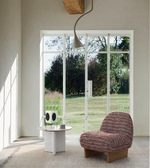 Modern lounge area with a textured accent chair, round side table, and large window view