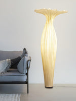Tall sculptural floor lamp with soft golden glow beside modern sofa