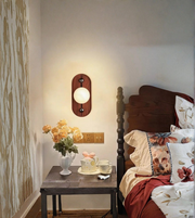 Wooden wall sconce with glowing round glass globe in bedroom setting