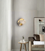 Modern wall sconce on a gray wall with a chair and small table in the foreground.
