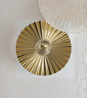 Close-up of a gold decorative wall piece against a white wall.