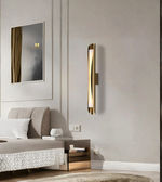 Modern bedroom with a gold wall sconce, bed, and mirror.