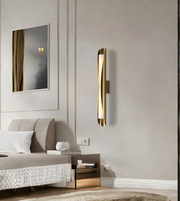 Modern bedroom with a gold wall sconce, bed, and mirror.