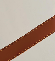 Close-up of a brown leather strap with visible stitching on a light gray background
