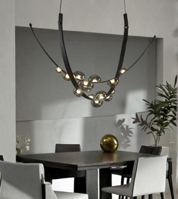 Modern chandelier hanging above a dining table with chairs in a minimalistic room.