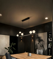 Modern interior with a long linear pendant light fixture in a darkly decorated room.