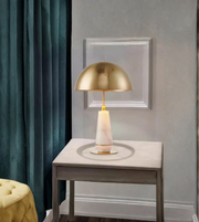 Gold table lamp on a white table against a gray wall with a framed picture.