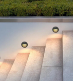 Modern outdoor wall lights on a concrete wall with greenery above.