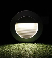 Round ground light emitting a bright white glow on grass with a dark background