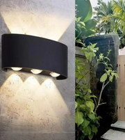 Black outdoor wall light fixture on a textured wall with a garden scene in the background.