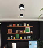 Black ceiling lights on a white ceiling with a shelf below displaying various items.