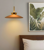 Modern pendant light fixture above a bed with a leaf-themed wall art piece.