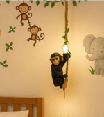 Decorative wall light shaped like a monkey hanging from a rope with wall stickers of monkeys and an elephant on a light-colored wall.