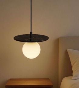 Modern pendant light with a round bulb hanging over a wooden nightstand in a bedroom setting.