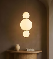 Modern pendant light with three spherical shades hanging above a wooden table with a vase and books.