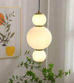 Modern pendant light with three spherical bulbs hanging in a room with a plant and wall art.