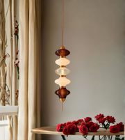Modern pendant light fixture with red roses on a wooden shelf against a neutral wall.