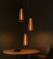 Three pendant lights hanging above a table with a bowl and chair in a dimly lit room.