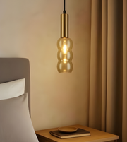 Gold pendant light hanging above a wooden nightstand with a bed in the background