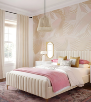 Neatly made bed with pink blanket and pillows in a bedroom with patterned wallpaper.
