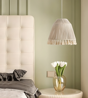 Neatly made bed with a white upholstered headboard, gray bedding, and a small table with a vase of white tulips against a green wall.