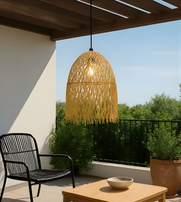Woven pendant light hanging above a patio table with a chair and plants on a sunny day.
