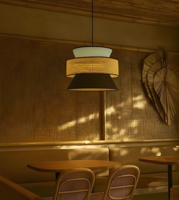 Dining area with wooden tables and chairs, illuminated by a pendant light with a woven design.