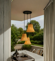 Woven pendant lights hanging over a table with a view of greenery outside.