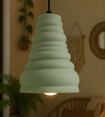 Green pendant light hanging in a room with plants and wall decor.