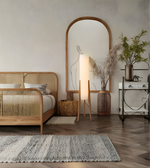 Modern wooden tripod floor lamp beside bed with fabric shade and warm ambient lighting