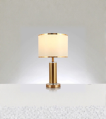Gold table lamp with fabric drum shade and metallic trim on white background
