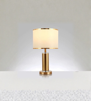 Gold table lamp with fabric drum shade and metallic trim on white background