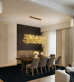 Modern dining room with a gold chandelier, wooden table, and gray chairs.