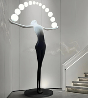 Modern sculpture of a woman with a circular light fixture above her head in an indoor setting.