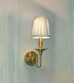 Wall-mounted lamp with a white shade and brass fixture on a light blue wall.