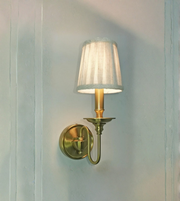 Wall-mounted lamp with a white shade and brass fixture on a light blue wall.