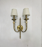 Brass wall sconce with two white lampshades on a light gray wall.