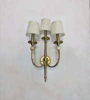 Brass wall sconce with three white lampshades on a light gray background