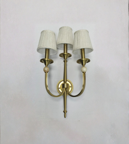 Brass wall sconce with three white lampshades on a light gray background