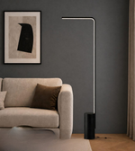 Modern floor lamp in a living room setting with a sofa and artwork on the wall.
