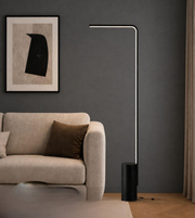 Modern floor lamp in a living room setting with a sofa and artwork on the wall.