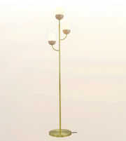 A modern floor lamp with a slim gold-finished metal stand, three curved arms, and three frosted white globe shades, shown against a plain light background.